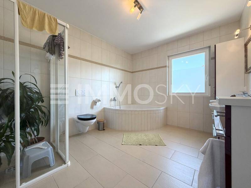 Geräumiges Badezimmer mit Badewanne, Duschkabine, Fenster und hellen Fliesen an Wänden und Boden.