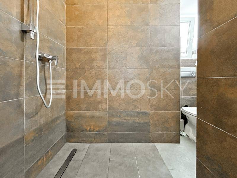 Modernes Badezimmer mit einer geräumigen, begehbaren Dusche und großformatigen Fliesen in Erdtönen.