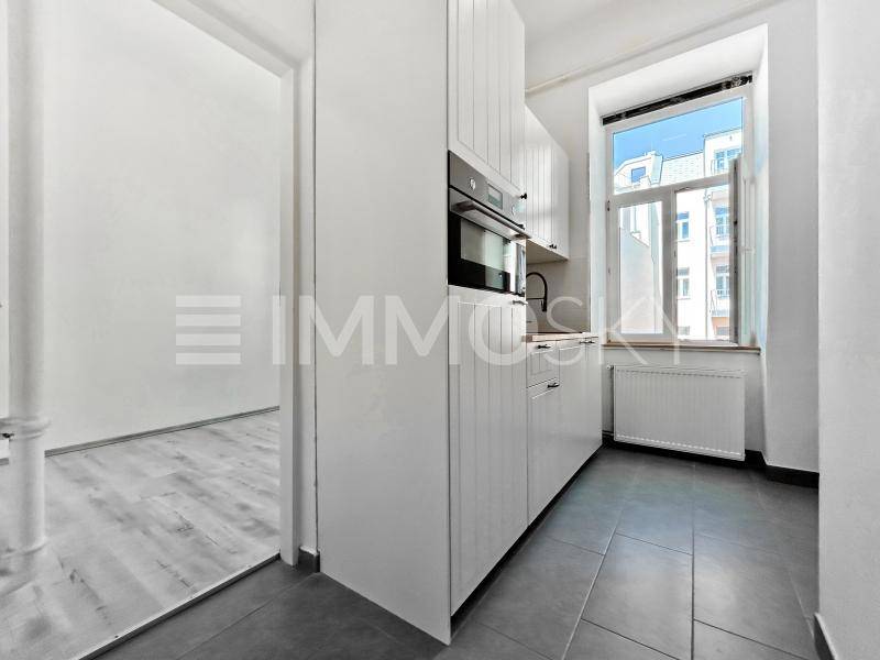 Moderne weiße Küche mit Einbaugeräten, dunklen Fliesen und einem Fenster mit Blick nach draußen.