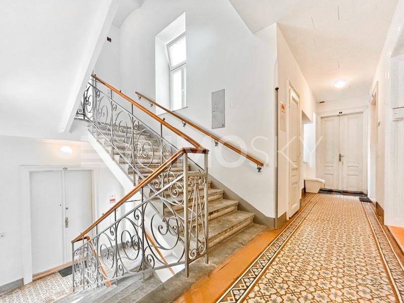 Elegantes Treppenhaus mit schmiedeeisernem Geländer und einem gemusterten Fliesenboden im Eingangsbereich.