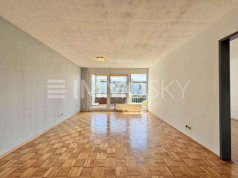 Geräumiges Wohnzimmer mit Parkettboden und Zugang zu einem Balkon, hell und unmöbliert.