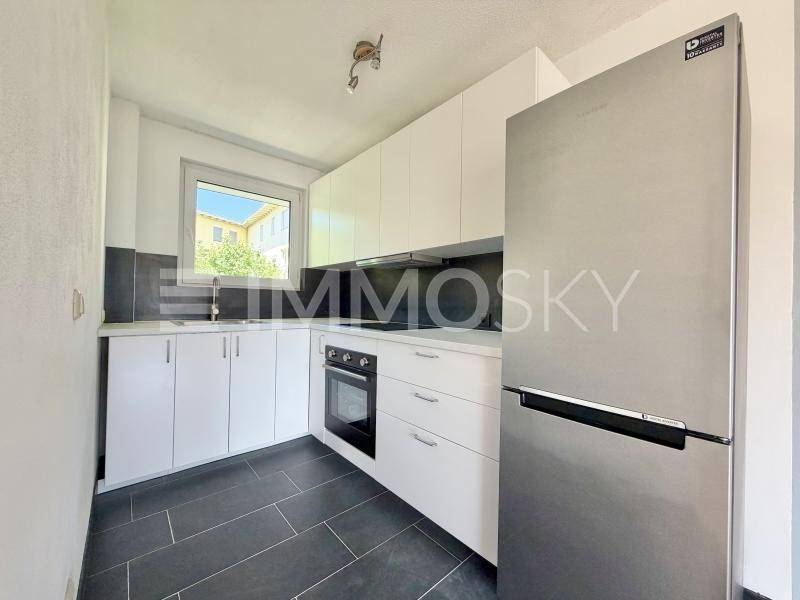 Moderne Küche mit weißen Schränken, dunklem Fliesenboden, Backofen und großem Kühlschrank.