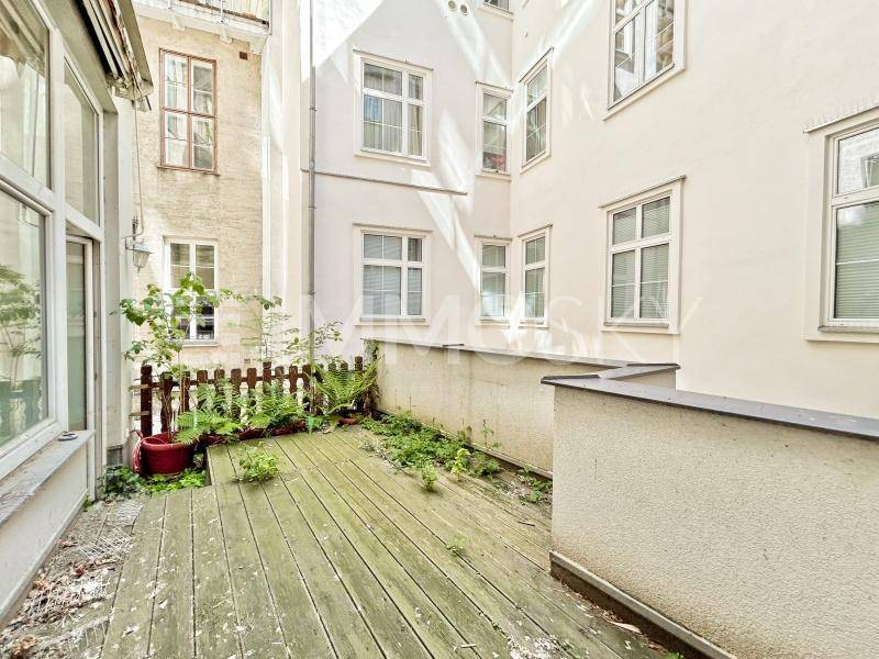 Eine kleine Holzterrasse im Innenhof mit Pflanzen, umgeben von Gebäudefassaden.