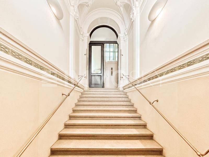 Elegantes Treppenhaus mit Marmorstufen, verzierten Wänden und einem hohen Bogen am Eingang.