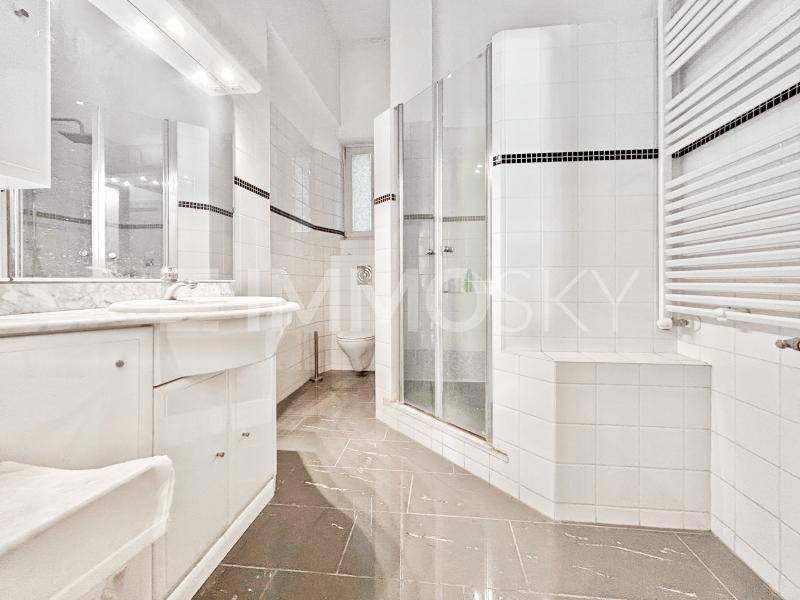 Helles Badezimmer mit weißen Fliesen, einer Duschkabine, Waschbecken und Handtuchheizkörper.