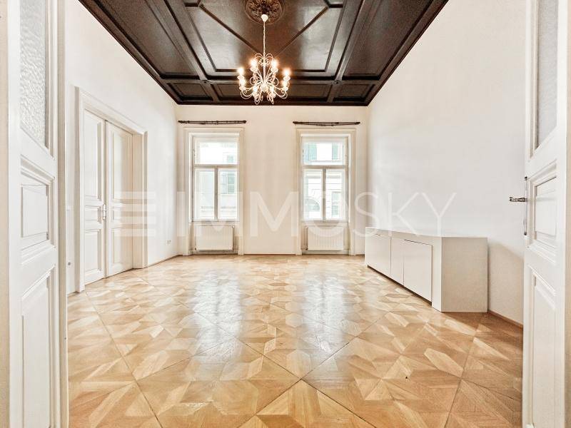 Geräumiges Zimmer mit kunstvollem Parkettboden, dunkler Kassettendecke und elegantem Kronleuchter.
