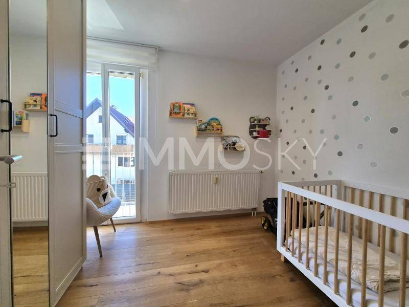 Helles Kinderzimmer mit Holzboden, Babybett und direktem Zugang zum Balkon.