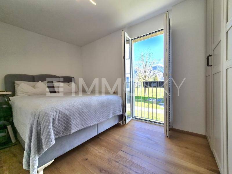 Schlafzimmer mit Doppelbett, Holzboden und Balkontür mit Bergblick.