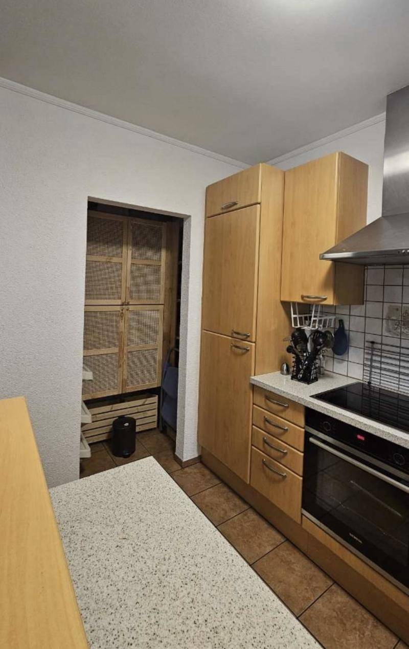 Funktionale Küche mit hellen Holzschränken, Kochfeld, Backofen und Dunstabzugshaube sowie Zugang zur Speisekammer.