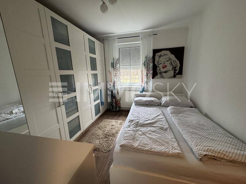 Helles Schlafzimmer mit großem weißen Kleiderschrank, Doppelbett und einem Fenster mit Rollladen.