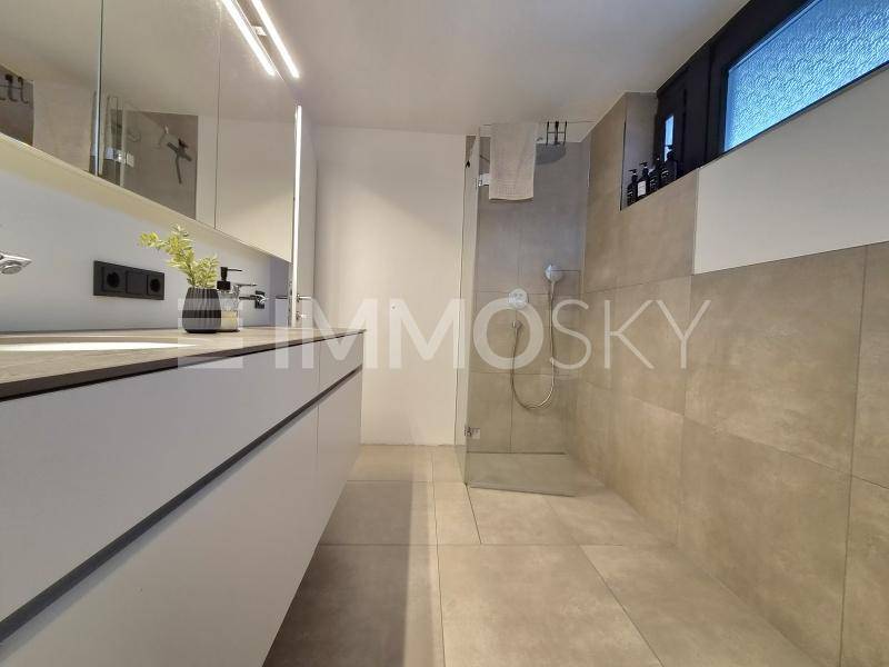 Modernes Badezimmer mit Doppelwaschbecken, großer begehbarer Dusche und beigefarbenen Fliesen.