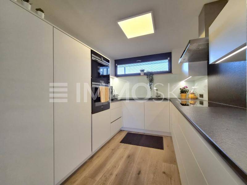 Moderne Küche mit weißen Schränken, dunklen Arbeitsplatten und integrierten Geräten sowie Fenster.