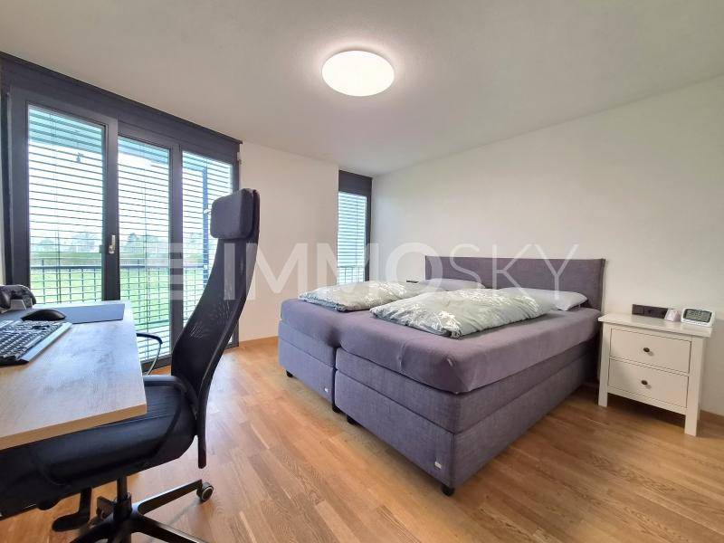 Helles Schlafzimmer mit Doppelbett, Schreibtisch und großen Fenstern mit Zugang zum Außenbereich.