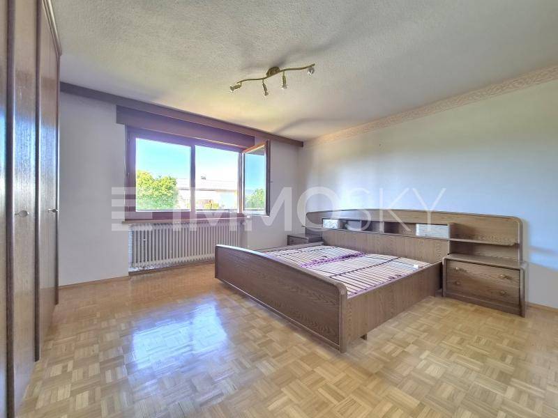 Geräumiges Schlafzimmer mit Holzbett, Nachttischen und großem Fenster für viel Tageslicht und Ausblick.