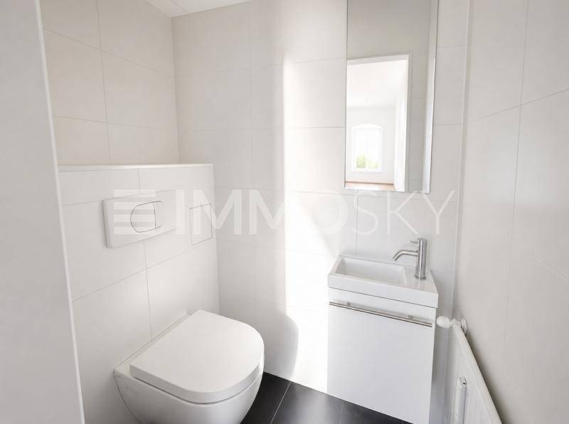 Helles Gäste-WC mit wandhängendem WC, kleinem Waschbecken und dunklen Bodenfliesen.