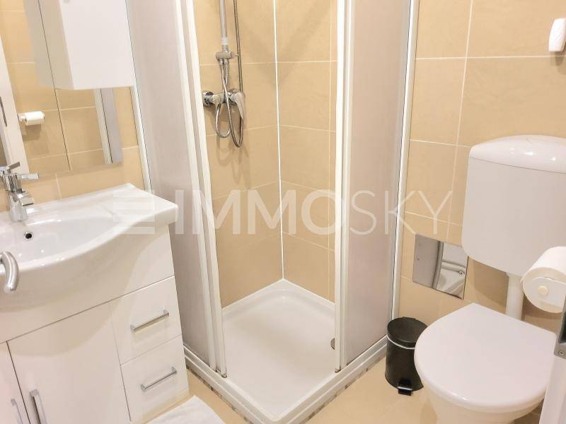 Kleines Badezimmer mit Duschkabine, WC, Waschbecken und hellen Fliesen.