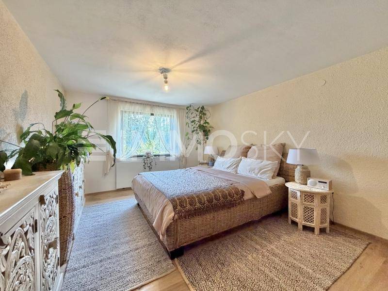 Schlafzimmer mit Korbbett, Nachttischen und vielen Pflanzen, hell und freundlich gestaltet.