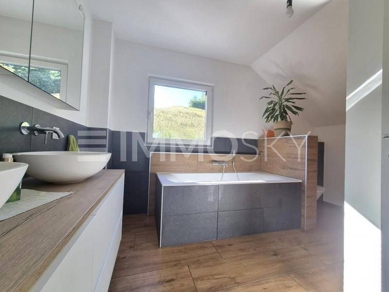Modernes Badezimmer mit Doppelwaschbecken, Badewanne und Fenster unter Dachschräge.