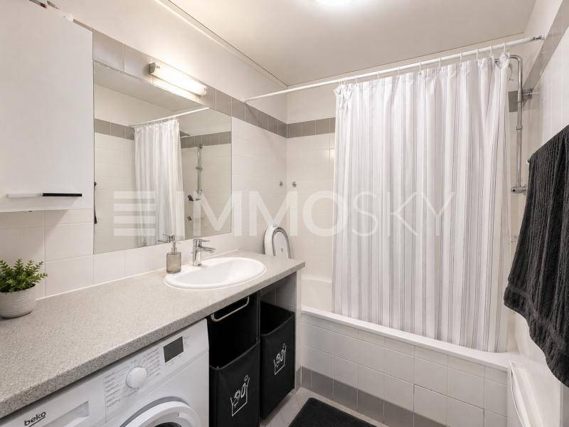 Modernes Badezimmer mit Badewanne, Duschvorhang, Waschbecken und Waschmaschine.
