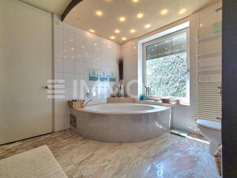 Modernes Badezimmer mit großer runder Badewanne, Fliesenboden und Deckenstrahlern.