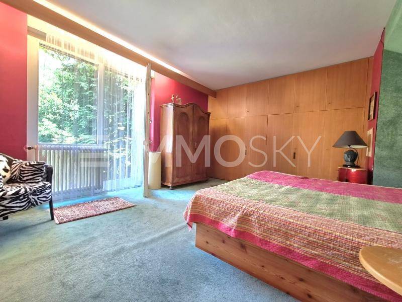 Schlafzimmer mit Holzbett, grüner Teppichboden, Einbauschränken und Zugang zum Außenbereich.
