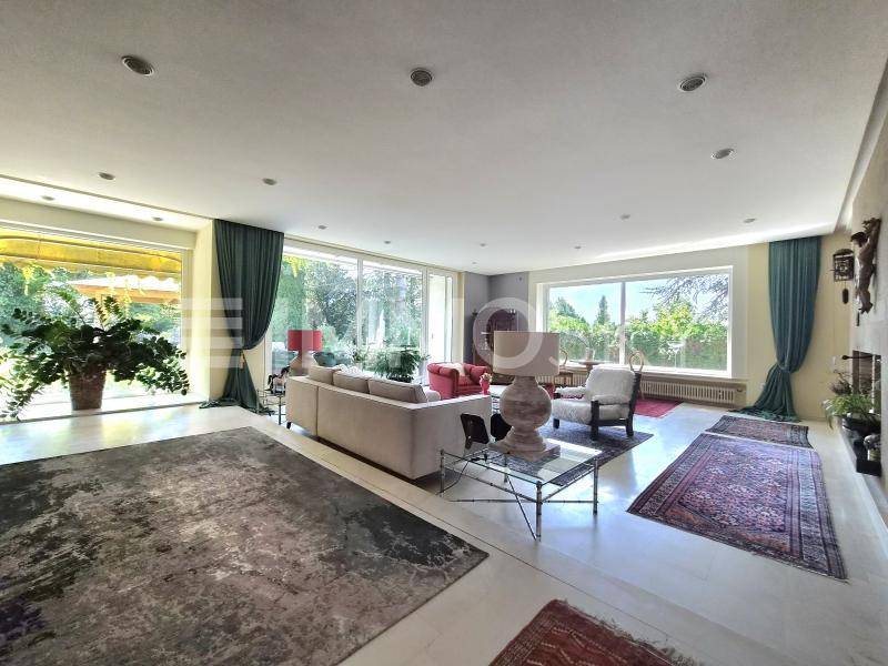 Helles und geräumiges Wohnzimmer mit großen Fenstern, Blick ins Grüne und eleganten Teppichen.