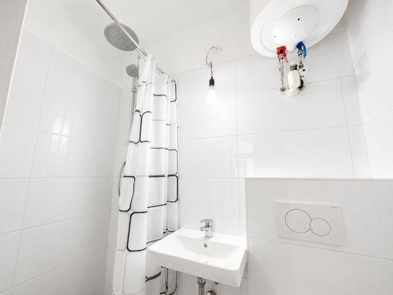Kleines, funktionales Badezimmer mit Dusche, Waschbecken und weiß gefliesten Wänden.