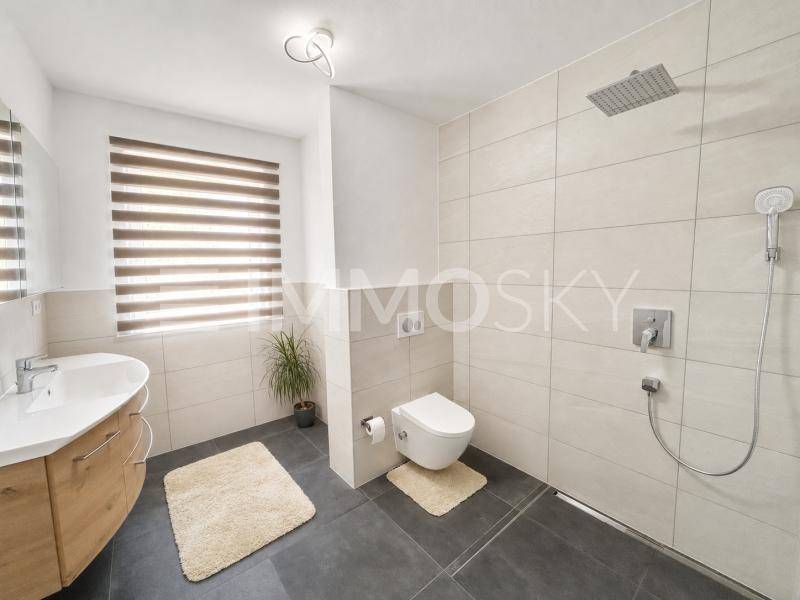 Modernes Badezimmer mit ebenerdiger Regendusche, Wand-WC, Holzwaschtisch und Fenster für Tageslicht.