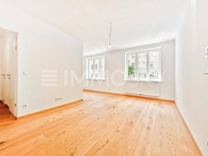 Geräumiges, helles Wohnzimmer mit neuem Holzparkett und Blick auf die umliegenden Gebäude.
