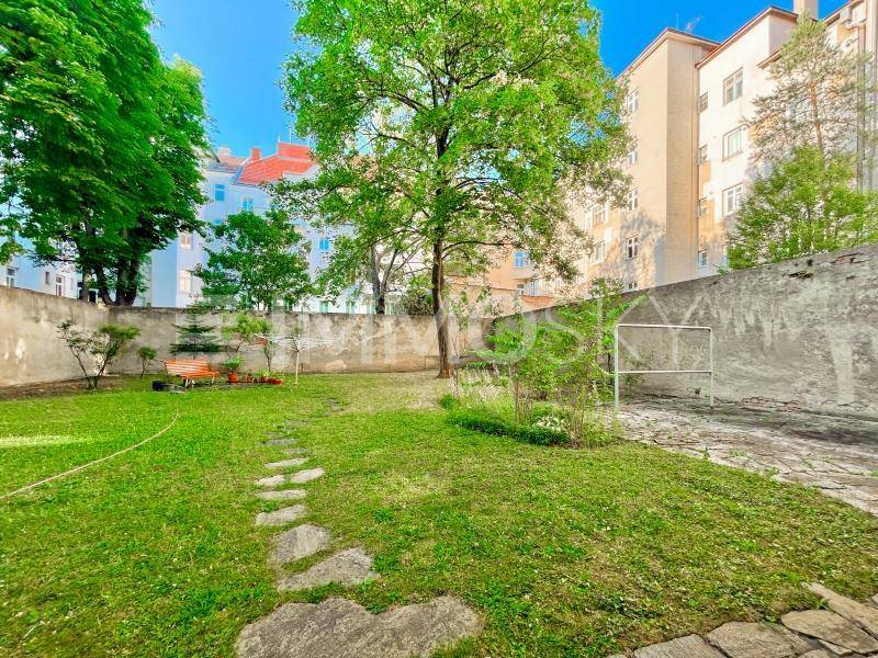 Grüner Gartenbereich mit Rasenfläche, Baumbestand und einer Holzbank, umgeben von einer Mauer.