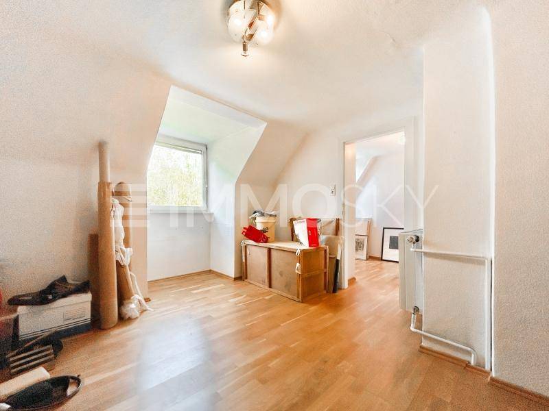 Dachgeschosszimmer mit schrägen Wänden, Holzboden und einem Fenster, das Tageslicht hereinlässt.