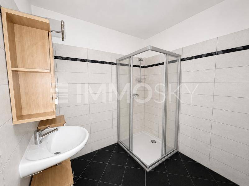 Helles Badezimmer mit Duschkabine, Eckwaschbecken und hellen Wandfliesen.