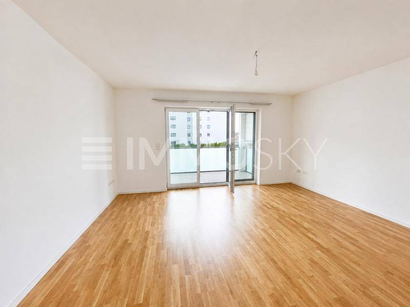 Geräumiges, leeres Wohnzimmer mit Holzparkettboden und Zugang zu einem Balkon.