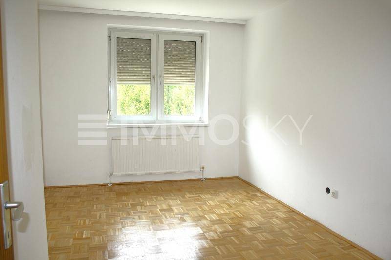 Leeres Schlafzimmer mit Parkettboden, einem Fenster und einem Heizkörper.