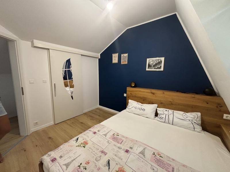 Schlafzimmer mit Holzbett, blauer Akzentwand und Dachschräge.