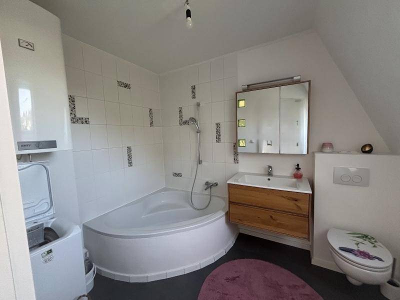 Helles Badezimmer mit Eckbadewanne, Holzwaschtisch und Dachschräge.