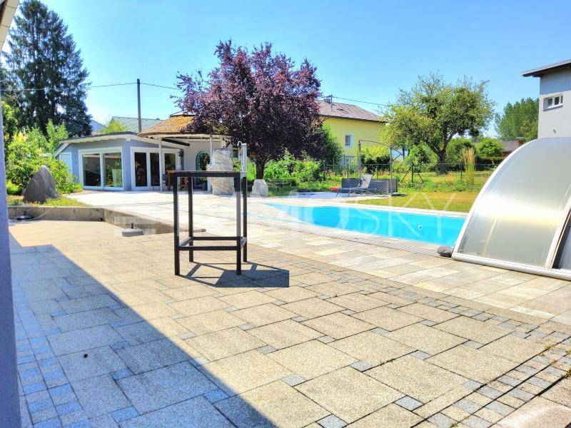 Großer Außenbereich mit Swimmingpool, gepflasterter Terrasse und viel Grünfläche.