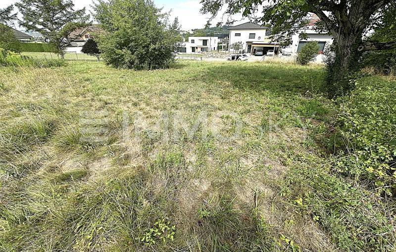 Unbebautes Grundstück mit üppigem Gras und Bäumen, umgeben von Wohnbebauung unter klarem Himmel.