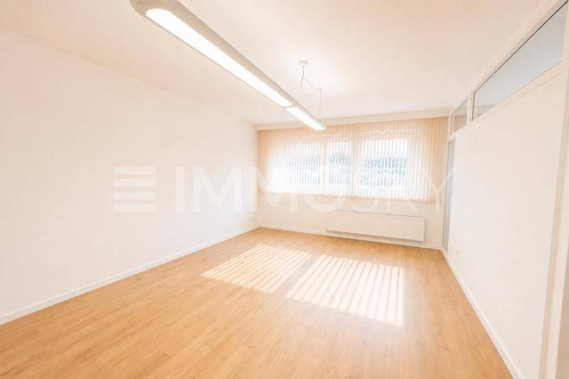 Leerer Büroraum mit hellem Laminatboden und großen Fenstern für viel Tageslicht.