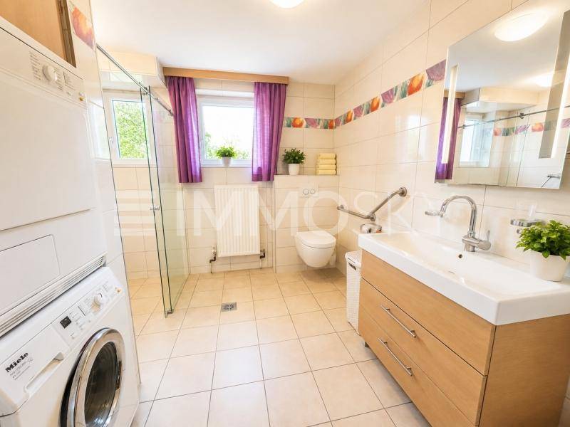 Modernes Badezimmer mit ebenerdiger Dusche, Waschmaschine und Trockner.