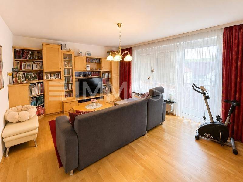 Gemütliches Wohnzimmer mit großem Sofa, Bücherregalen und Zugang zum Balkon.