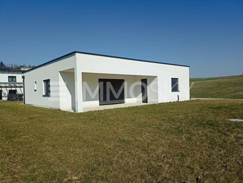 Rückansicht des modernen Hauses mit überdachtem Bereich und weitläufigem Rasen unter klarem Himmel.