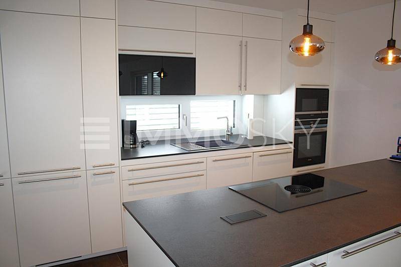 Moderne Einbauküche mit weißen Schränken, dunklen Arbeitsplatten, Kochinsel und integrierten Geräten.
