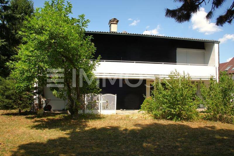 Rückseite des Hauses mit Balkon, dunkler Fassade und umgebender Natur.