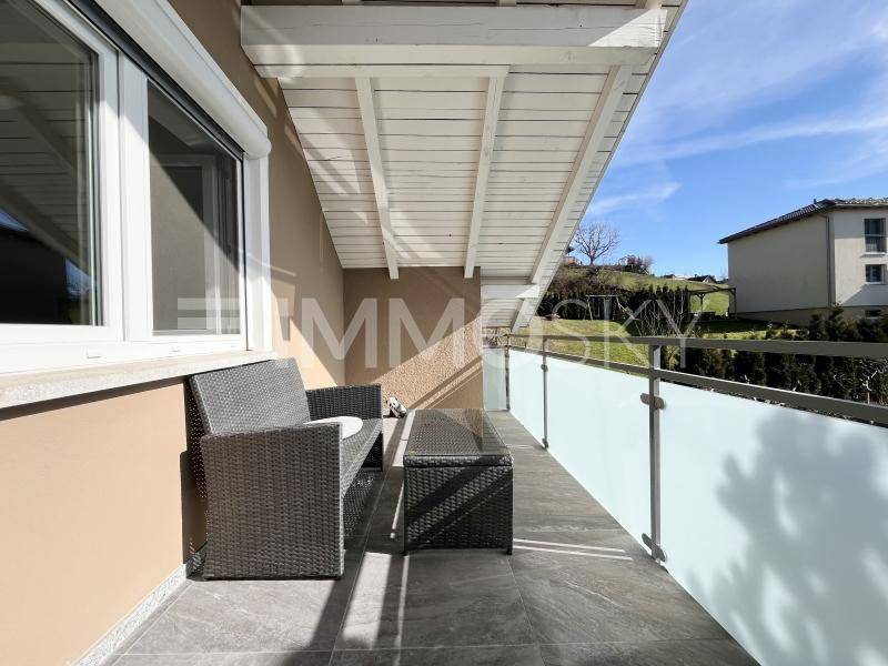 Überdachter Balkon mit modernen Outdoor-Möbeln und Blick ins Grüne.