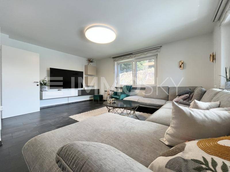 Modernes Wohnzimmer mit großem Ecksofa, dunklem Boden und viel Tageslicht.