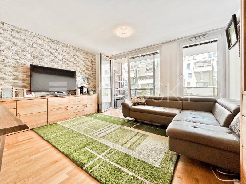 Gemütliches Wohnzimmer mit Holzboden, Steinwand und Zugang zu einem sonnigen Balkon.