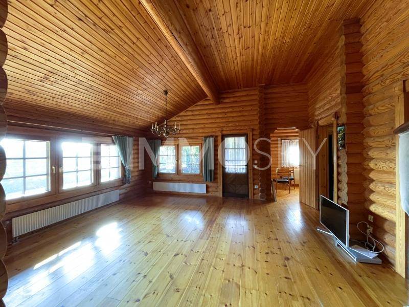 Geräumiges Wohnzimmer im Blockhausstil mit Holzböden, Holzverkleidung an Wänden und Decke sowie großen Fenstern.