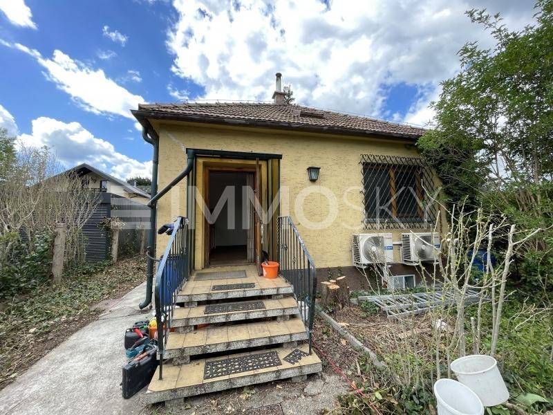 Einfamilienhaus mit gelber Fassade, Außentreppe und Klimaanlagen im Gartenbereich.