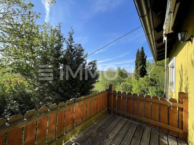 Sonniger Holzbalkon mit rustikalem Geländer und weitem Blick über die grüne Landschaft.